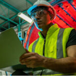 heavy equipment manufacturing employee wearing a hard hat and using a laptop | Finding the Right LMS as a Heavy Equipment Manufacturer